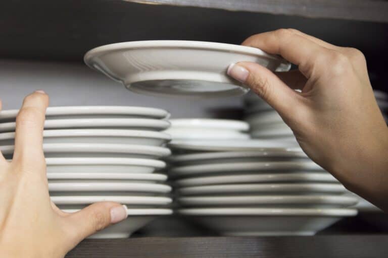 Cropped image of a woman's hands organising plates on a shelf in the concept of 'How to Pack Fragile Items'.